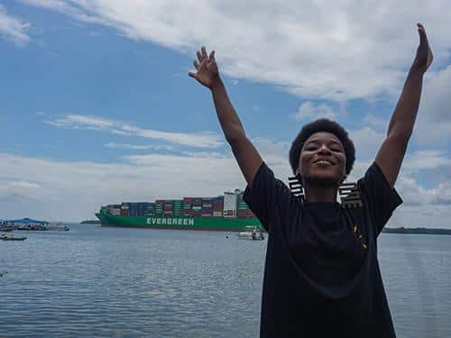 Mujer con los brazos abiertos y buque carguero detras